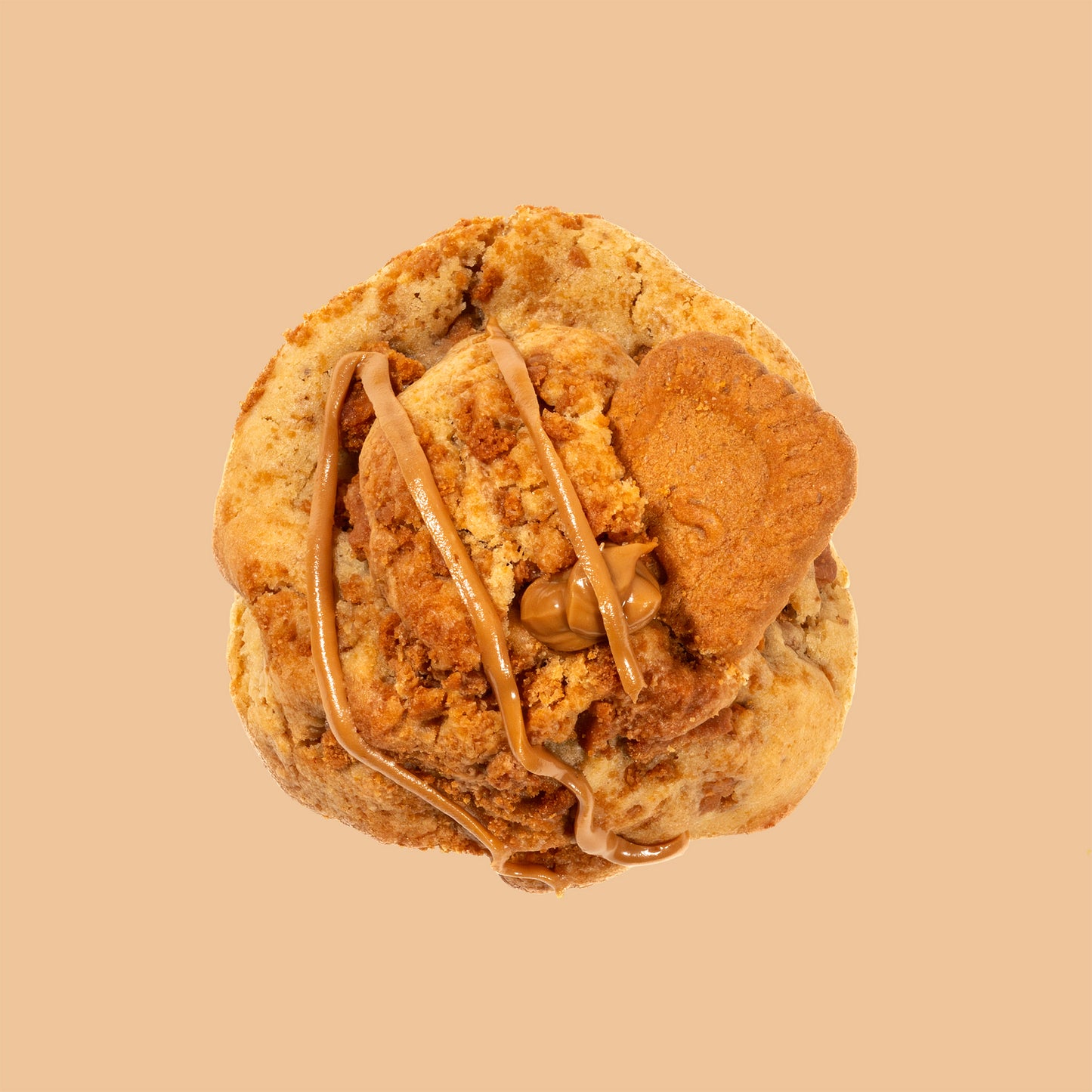 Cookie artisanal au spéculos vu de dessus, décoré d'un filet de pâte de spéculos lotus et d'un biscuit et brisures de spéculos croustillant sur fond beige orangé chaud. Texture moelleuse et dorée
