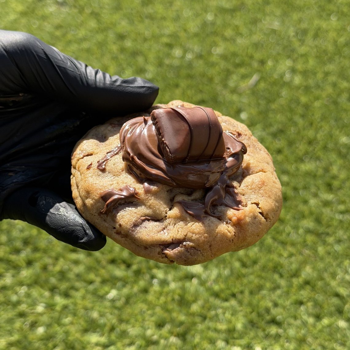 Cookie Bueno Nutella fait maison entier, tenu à la main, avec le milieu fondant de Nutella et morceau de Kinder Bueno bien visible, révélant un cœur fondant et coulant avec du chocolat au lait belge Callebaut et un morceau de Kinder Bueno entier posée sur le dessus, sur fond végétal vert.