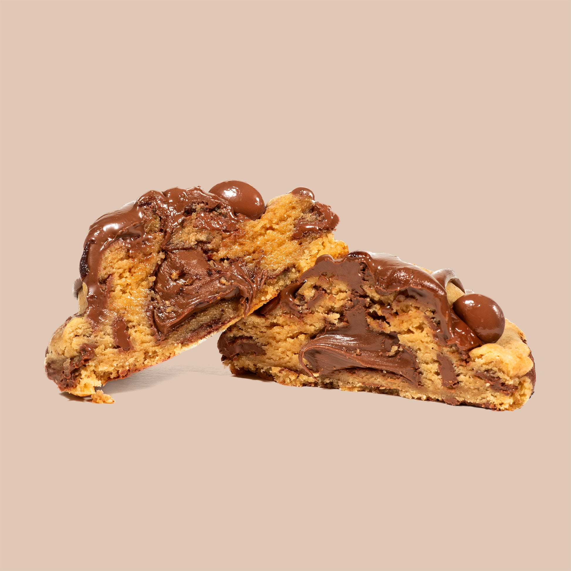 Cookie artisanal au Nutella coupé en deux, dévoilant un cœur fondant et généreux de pâte à tartiner chocolat noisette, pépites de chocolat au lait Callebaut sur fond clair. Texture moelleuse et ultra gourmande