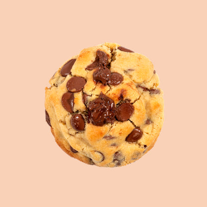 Cookie artisanal à l'Ovomaltine vu de dessus, doré et moelleux, garni de généreuses pépites de chocolat au lait Callebaut et d'un cœur croustillant chocolat malté, présenté sur fond beige pastel doux
