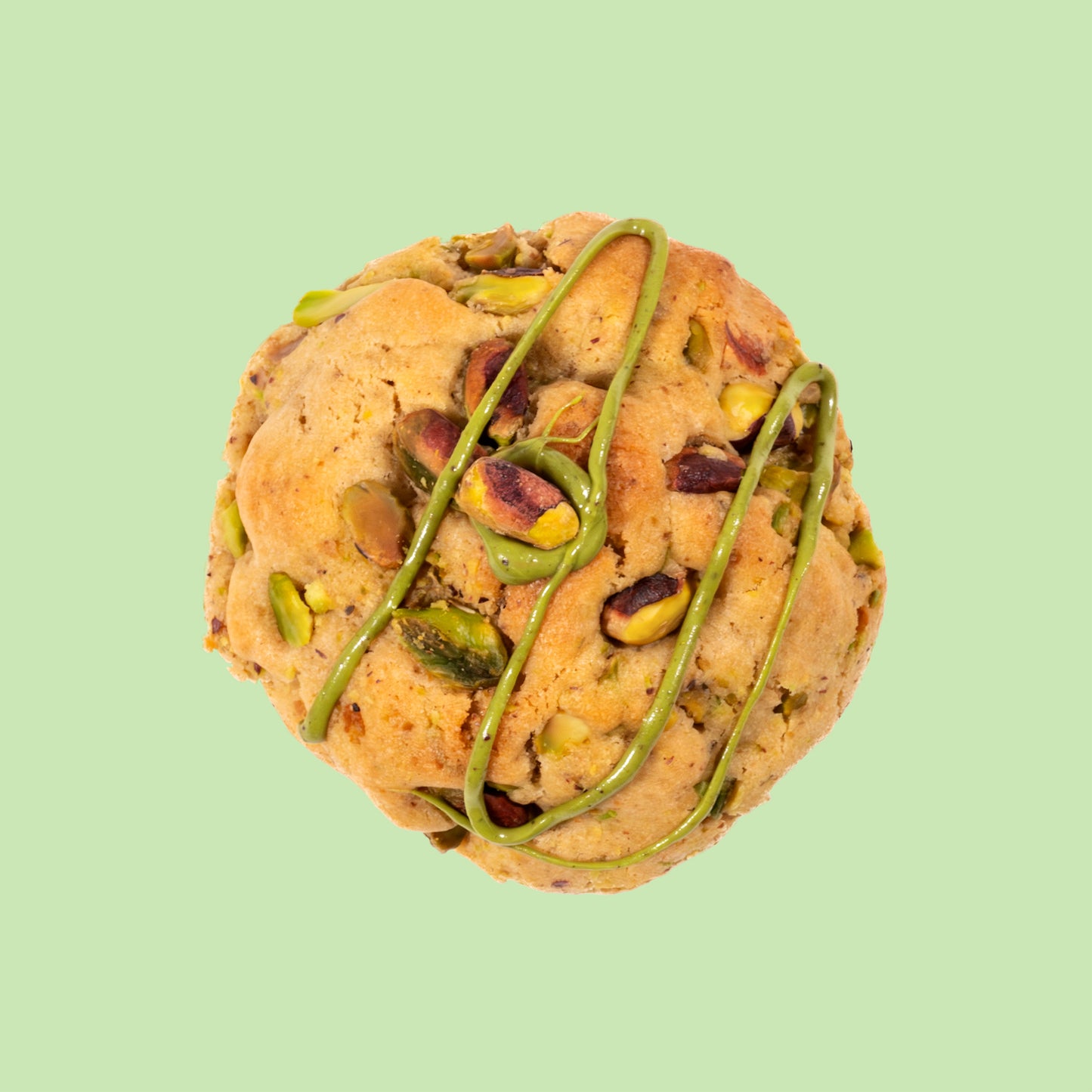 Cookie artisanal à la pistache vu de dessus décoré d'un filet de crème de pistache et garni d'éclats de pistaches entières sur fond clair
