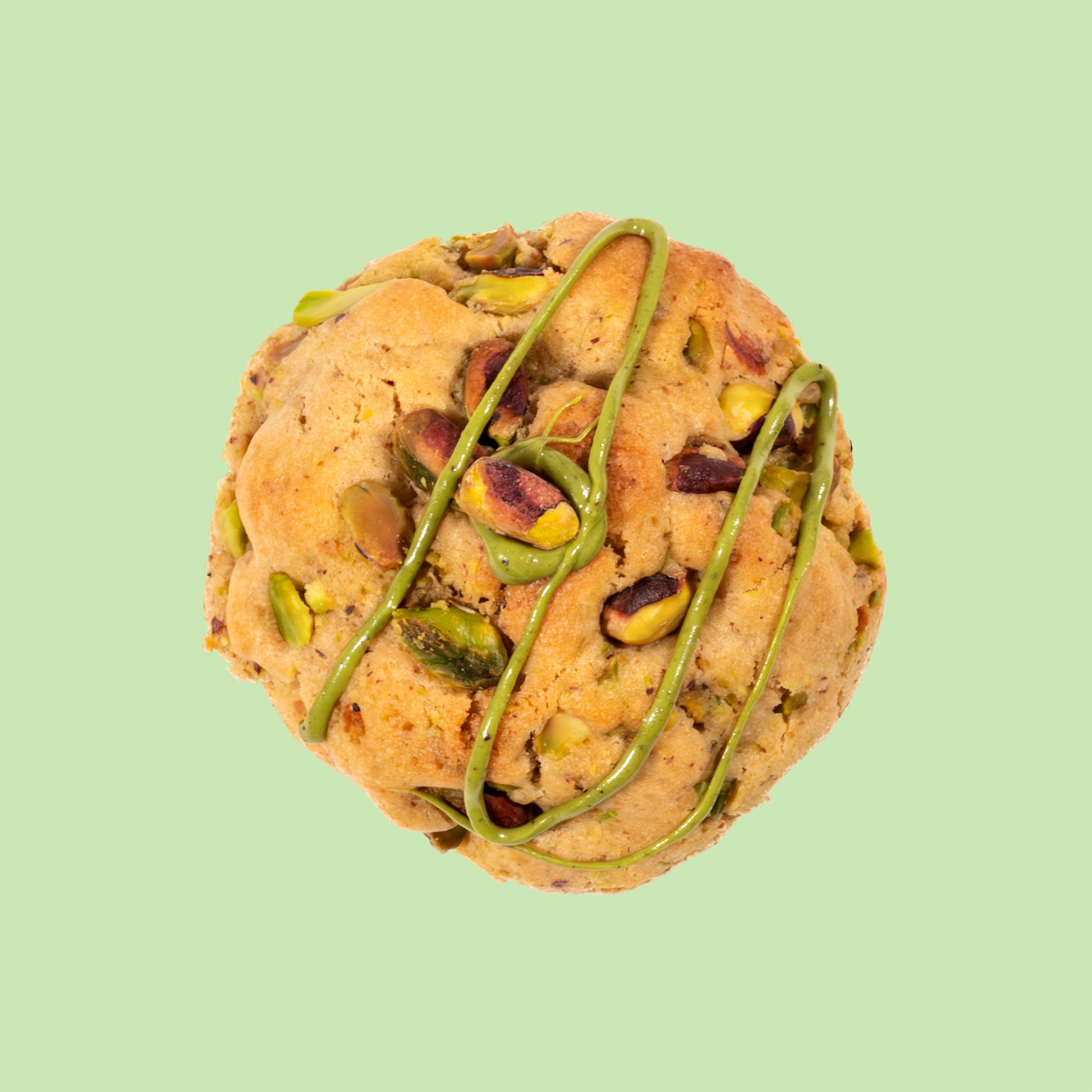 Cookie artisanal à la pistache vu de dessus décoré d'un filet de crème de pistache et garni d'éclats de pistaches entières sur fond clair