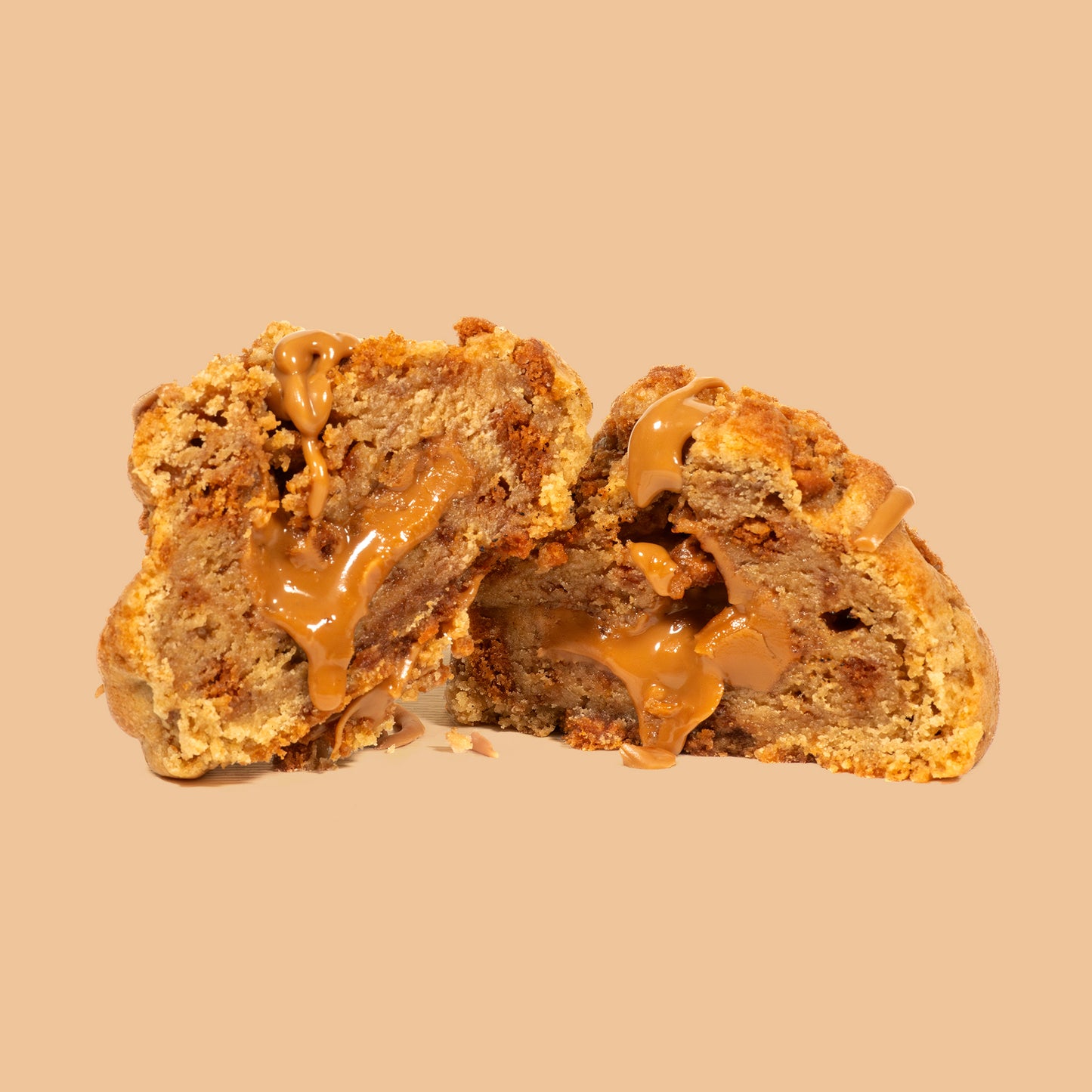 Cookie artisanal au spéculos coupé en deux, dévoilant un cœur fondant et coulant de pâte de spéculos, morceaux de biscuits sur fond beige orangé chaud. Texture moelleuse et gourmande