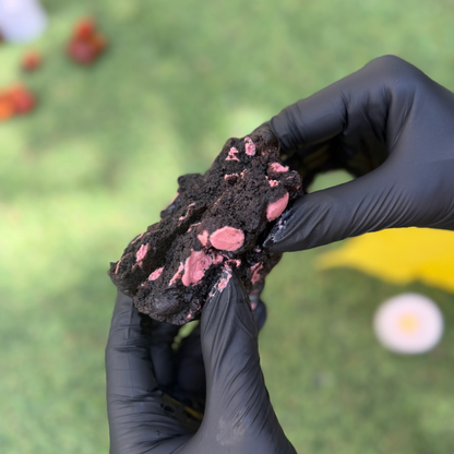 Cookie artisanal Halloween ouvert en 2 au cacao noir Callebaut garni de chocolat ruby Callebaut, tenu avec 2 mains, avec une texture moelleuse et fondante sur fond végétal 